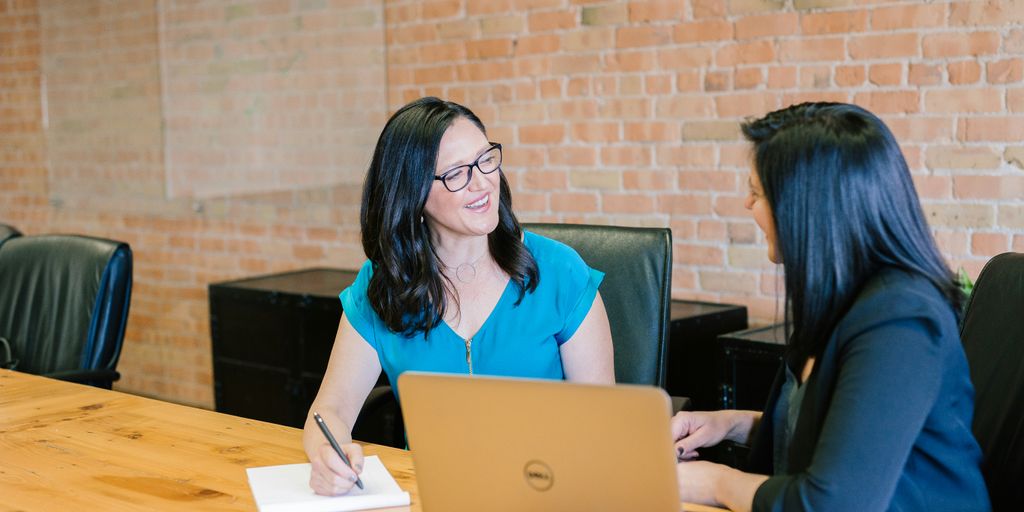 woman in teal t-shirt sitting beside woman in suit jacket