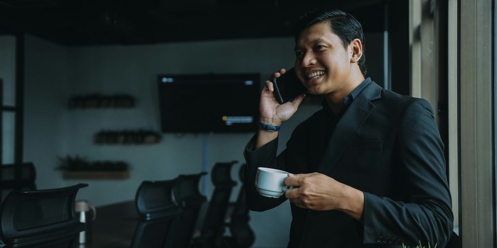 smiling man holding cup and using smartphone