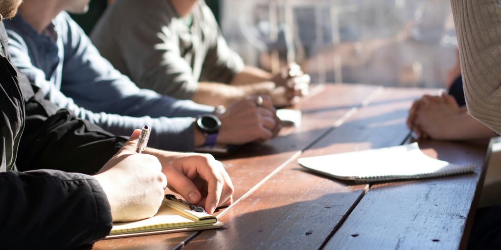 people sitting on chair in front of table while holding pens during daytime