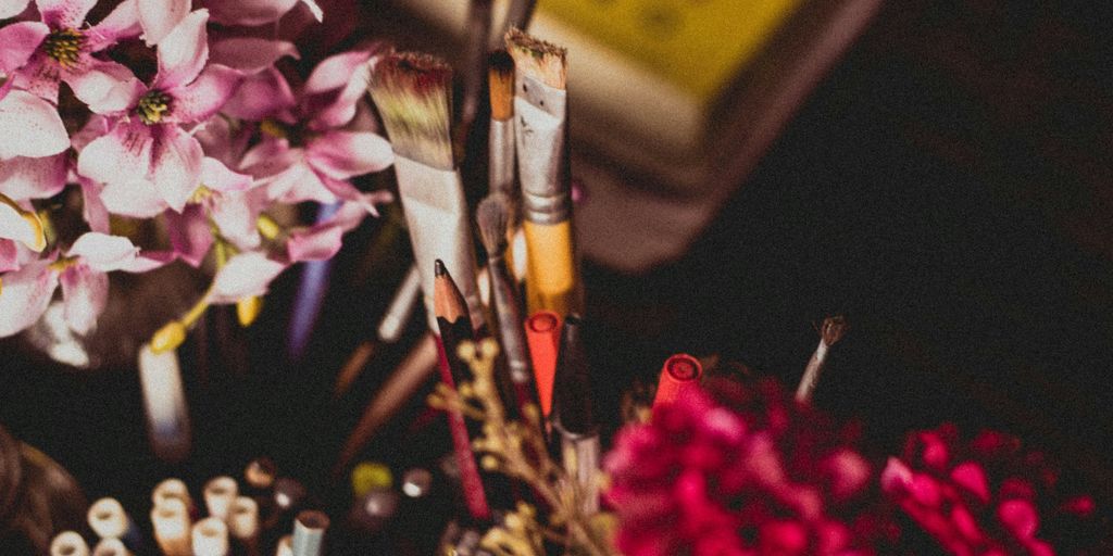 selective focus photography of makeup brush and pencil and pens beside pink and purple flowers